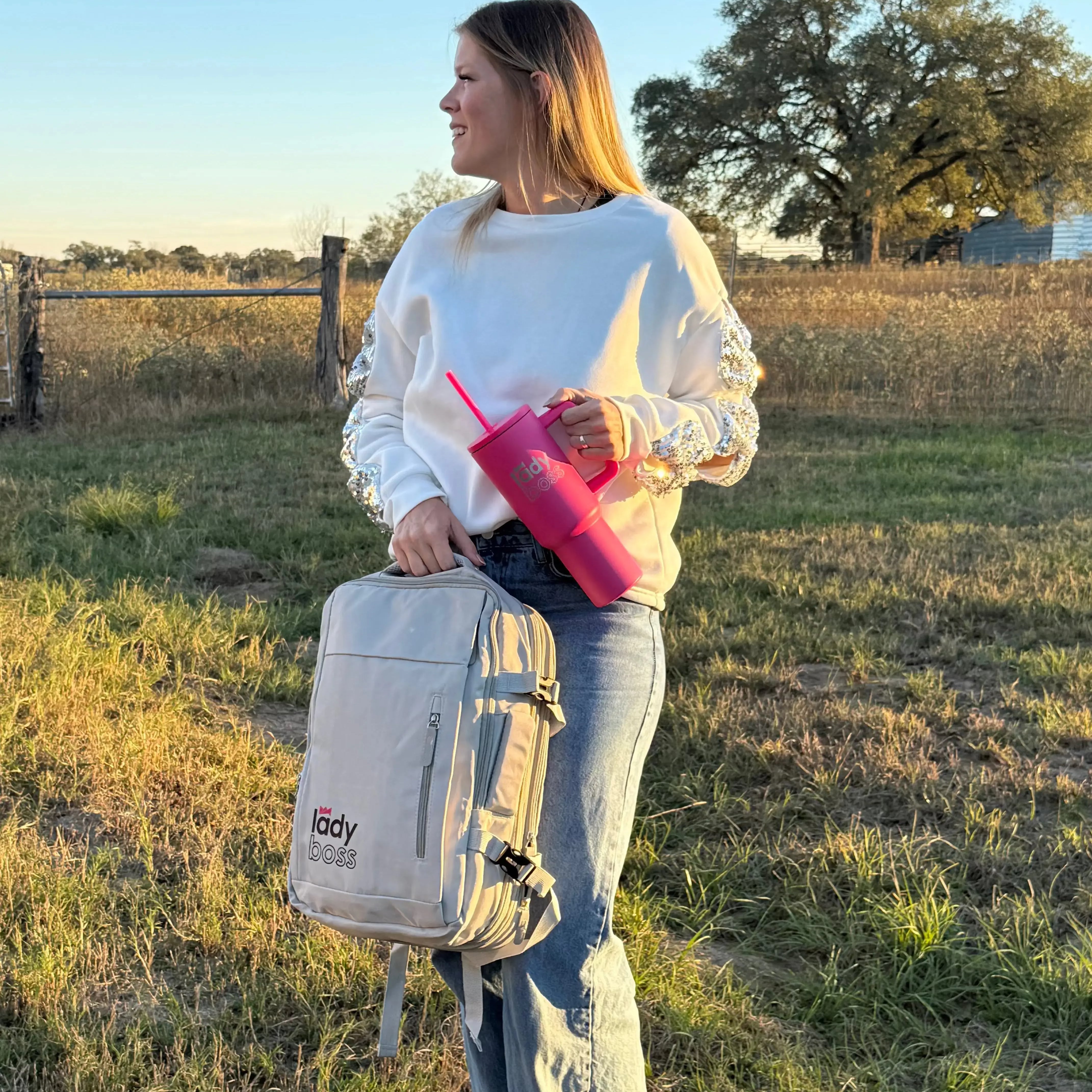 Woman holding a backpack and pink tumbler in a field