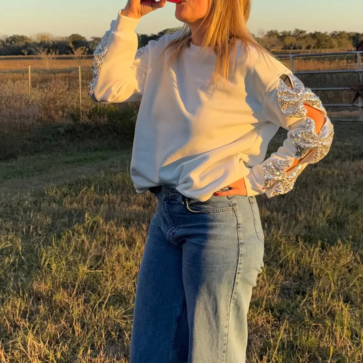 Person drinking from a red cup in a field with a clear sky