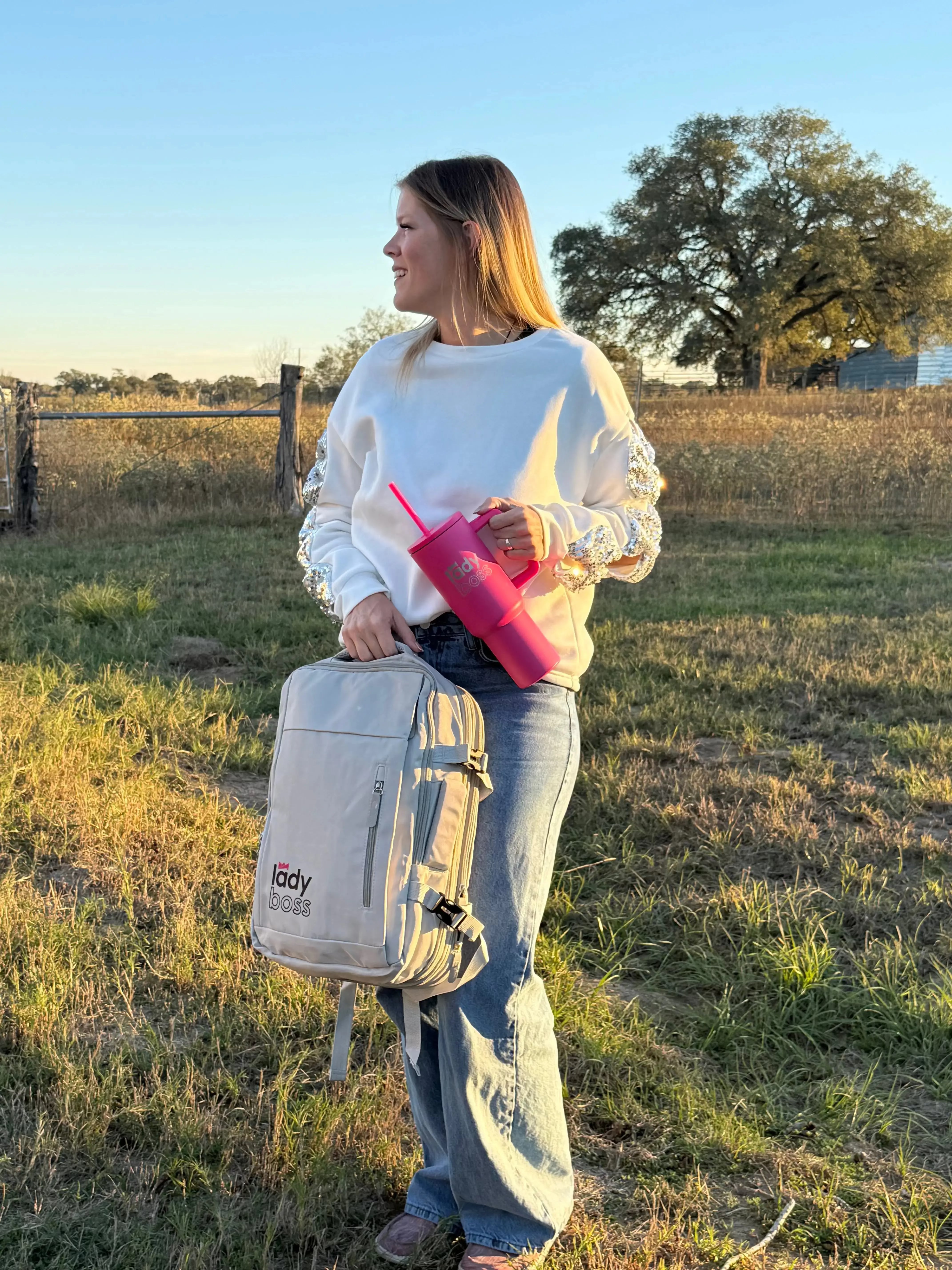 Woman holding a backpack and pink tumbler in a field