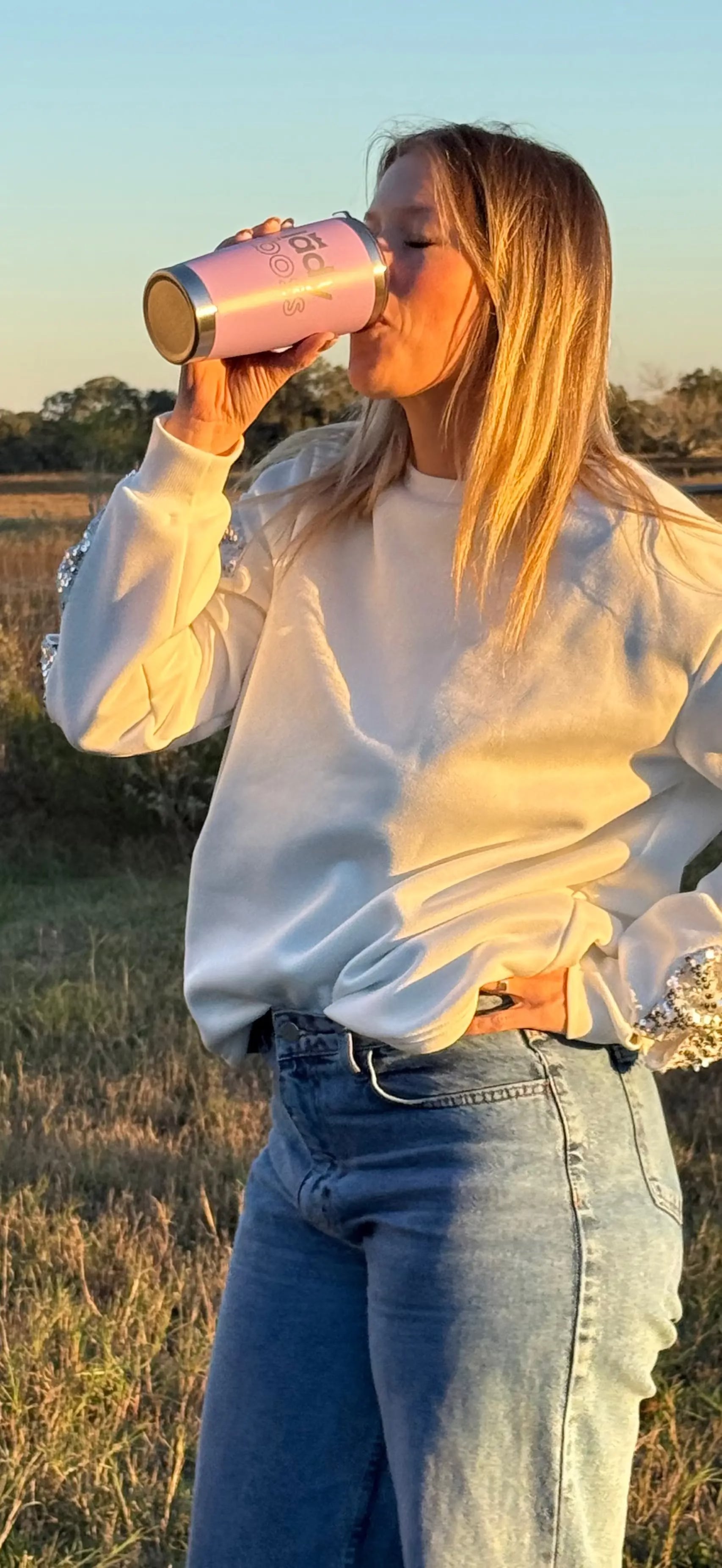 Person drinking from a pink cup in a field at sunset