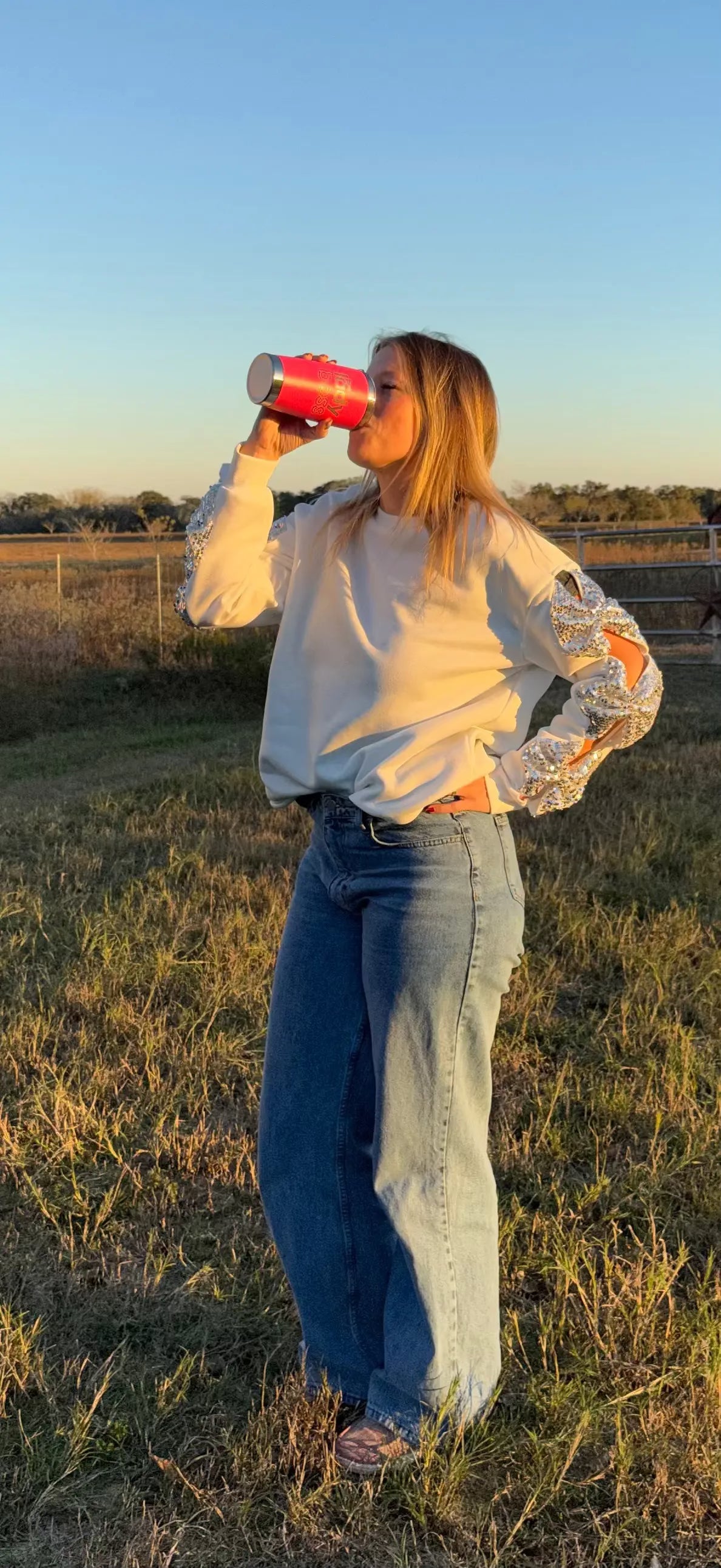 Person drinking from a red cup in a field with a clear sky